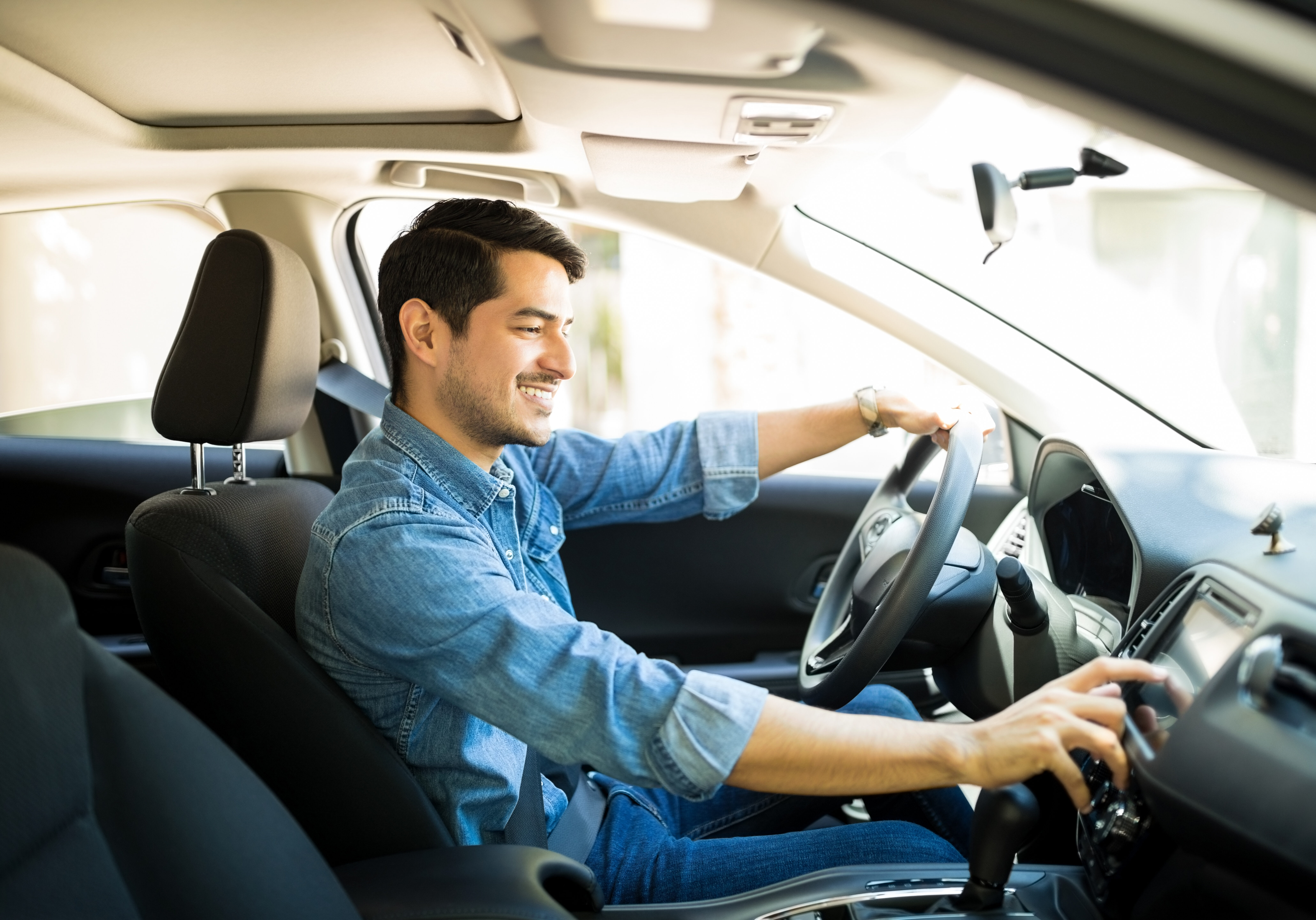 Handsome young man in denim shirt pressing touchscreen on car multimedia panel, switching shifting radio station.